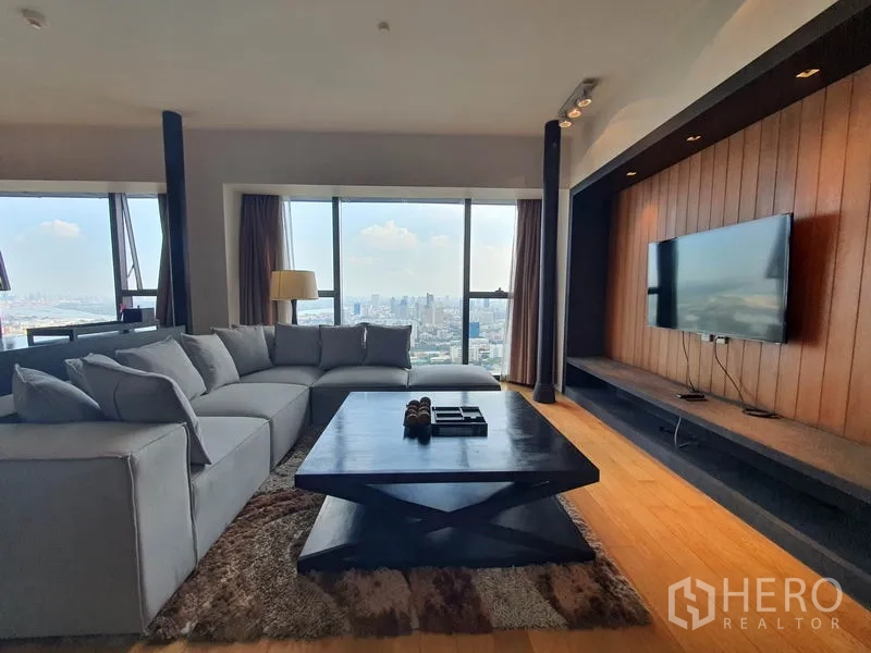 Condominium for rent in Sathon, Bangkok - Spacious living room with sectional sofa, TV wall and floor-to-ceiling windows overlooking Bangkok skyline.