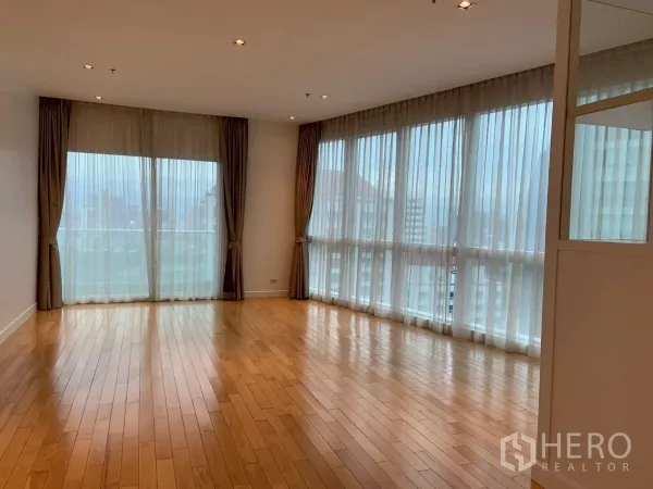 Condominium for rent in Khlong Toei, Bangkok - Spacious living area with panoramic windows and balcony access under recessed lighting.