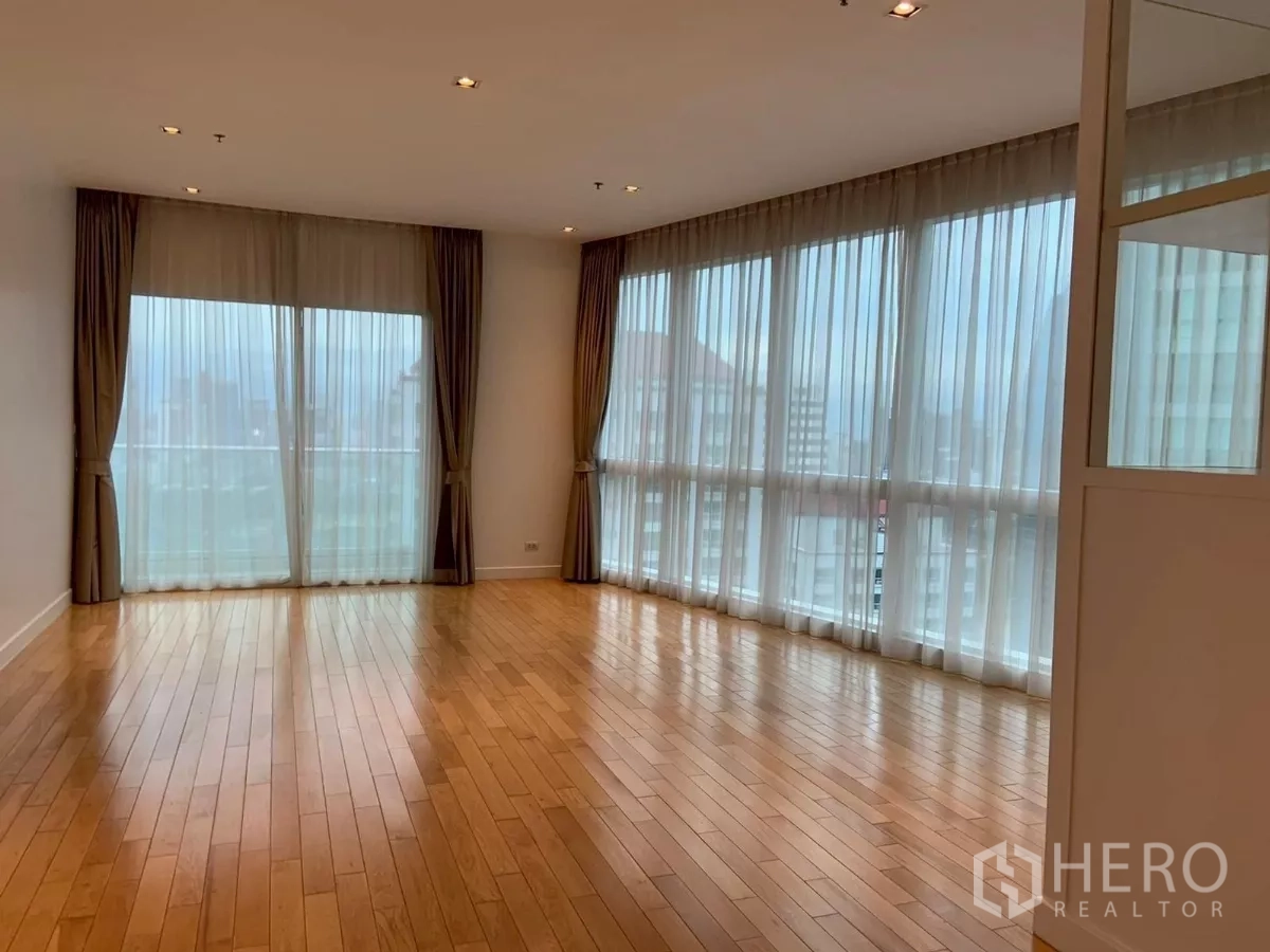 Condominium for rent in Khlong Toei, Bangkok - Spacious living area with panoramic windows and balcony access under recessed lighting.