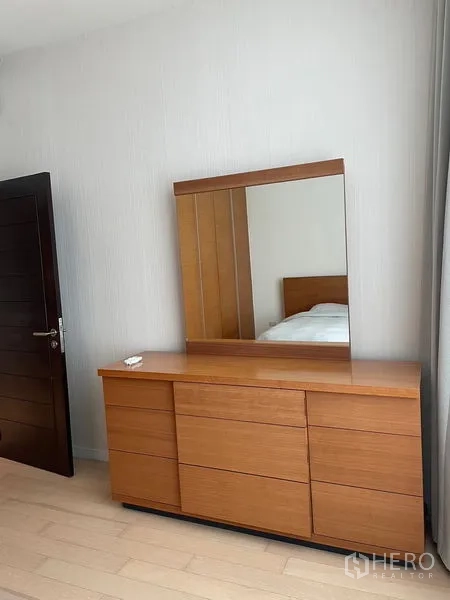 公寓 出租在Watthana, Bangkok - 卧室内的木质梳妆柜与大镜面，搭配木地板的现代公寓。