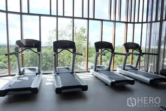คอนโด ให้เช่าหรือขาย - ห้องฟิตเนส มีลู่วิ่งเรียงสี่เครื่อง หน้าต่างสูงจรดเพดานมองเห็นวิวต้นไม้