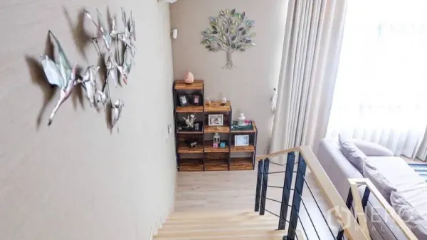 Townhouse for rent or sale in Suan Luang, Bangkok - Bright stair landing with decorative wall art, wood shelving and floor-to-ceiling curtains.