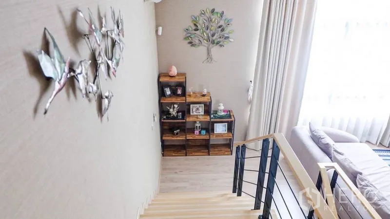 Townhouse for rent or sale in Suan Luang, Bangkok - Bright stair landing with decorative wall art, wood shelving and floor-to-ceiling curtains.