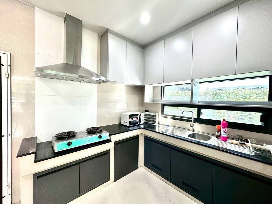 Detached House for rent in Bang Kapi, Bangkok - L-shaped kitchen with gas hob, stainless hood and sink beneath a long window.