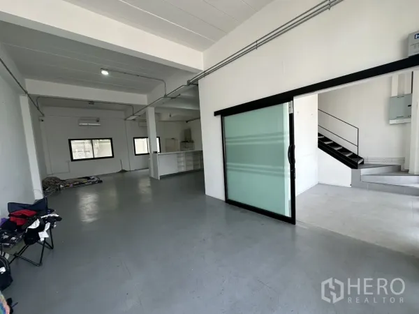 Home Office for rent or sale in Bang Na, Bangkok - Open-plan ground floor with grey flooring, sliding glass partition and metal staircase.