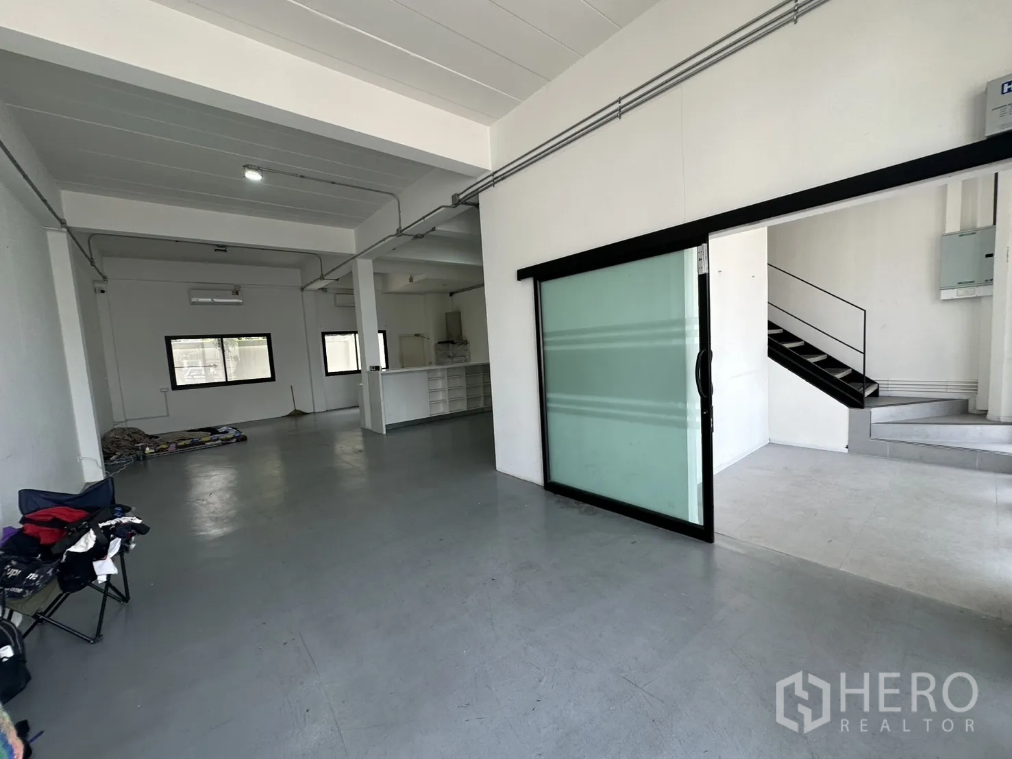 Home Office for rent or sale in Bang Na, Bangkok - Open-plan ground floor with grey flooring, sliding glass partition and metal staircase.