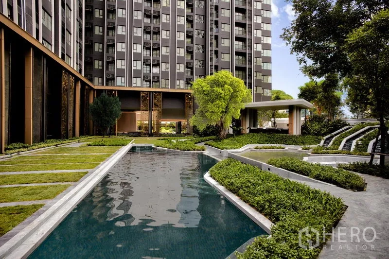 公寓 出租在Pathum Wan, Bangkok - 庭院泳池与草坪树木相伴，背景为现代高层公寓外立面。