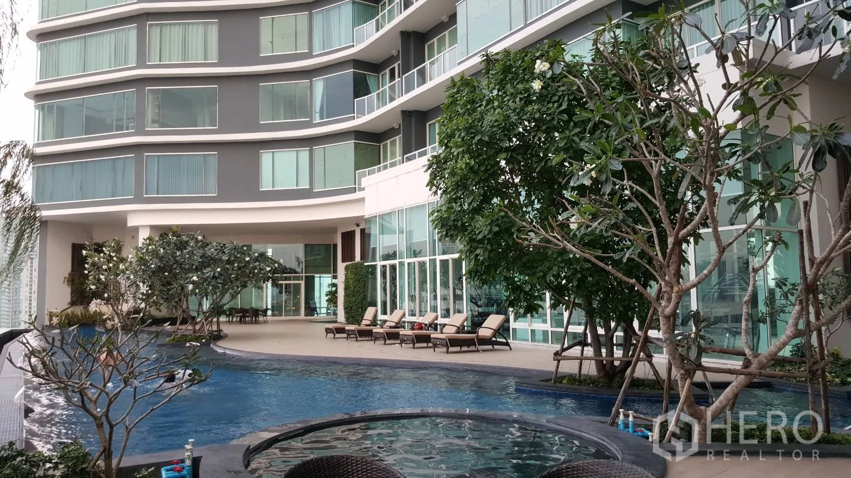 Condominium for rent in Bang Kho Laem, Bangkok - Curved modern condominium facade with landscaped pool deck, jacuzzi and sunbeds next to a glass-walled lobby.