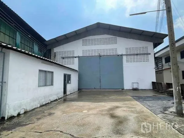 Warehouse for rent in Mueang Samut Sakhon, Samut Sakhon - Warehouse exterior with oversized double steel sliding door, concrete loading yard and a small attached office.