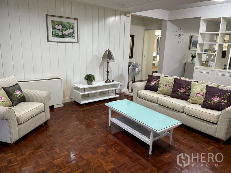 Apartment for rent in Watthana, Bangkok - Living room with striped sofa set, glass coffee table and wooden flooring.