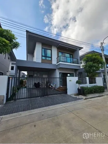 Detached House for sale in Khan Na Yao, Bangkok - Modern two-storey detached house facade with balcony, gated carport and small trees.