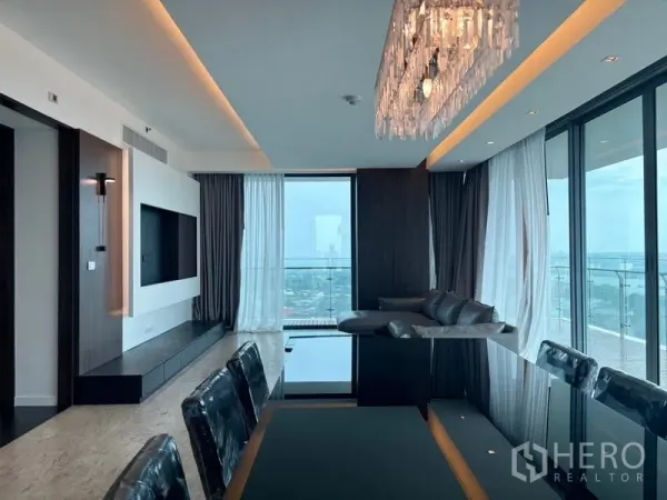 คอนโด ให้เช่า - ห้องนั่งเล่นและทานอาหารแบบโอเพ่นพร้อมโคมระย้า ผนังกระจกสูงจรดเพดานและระเบียง มองเห็นวิวเมืองและแม่น้ำเจ้าพระยา