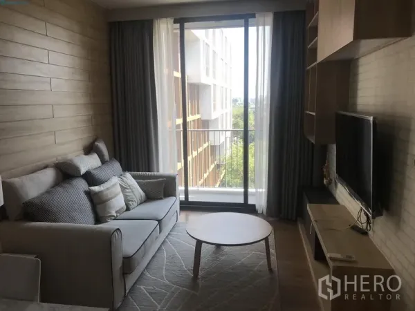 公寓 出租在Watthana, Bangkok - 客厅设电视柜与沙发，落地推拉门通向阳台，可见绿意景观。