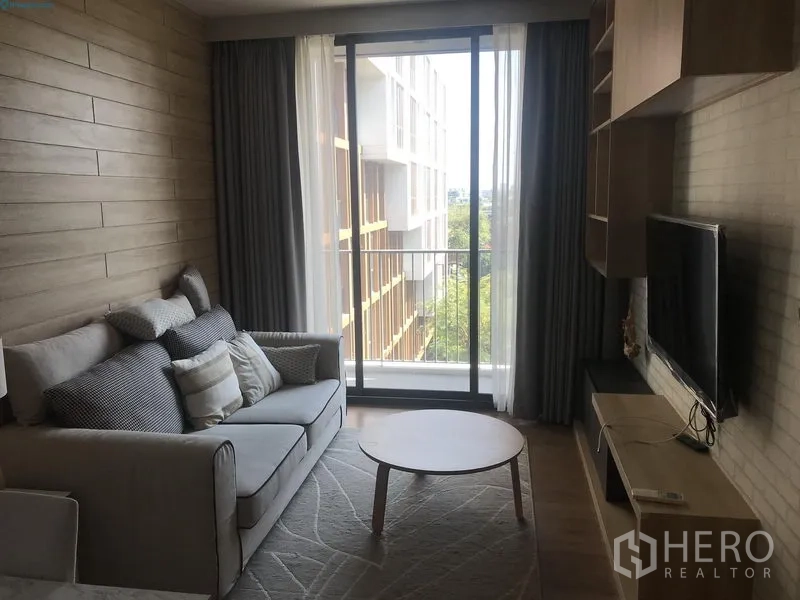 公寓 出租在Watthana, Bangkok - 客厅设电视柜与沙发，落地推拉门通向阳台，可见绿意景观。