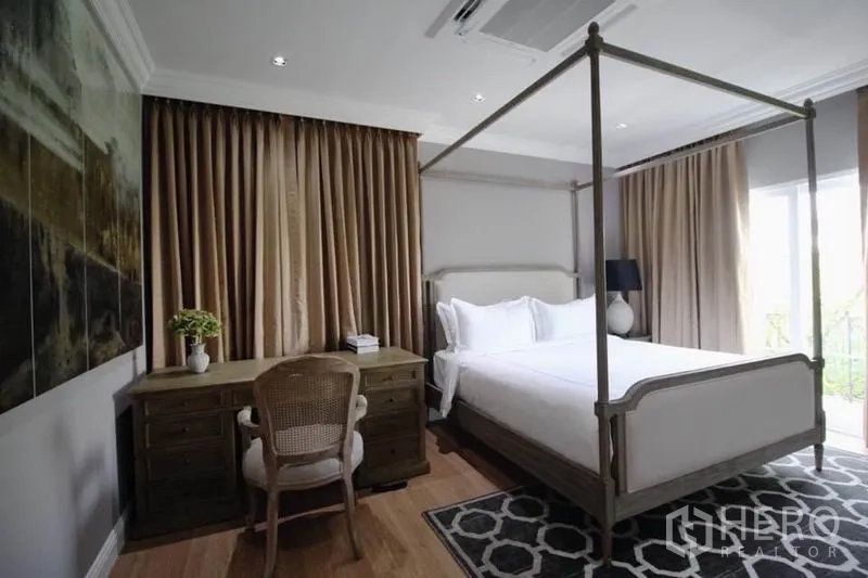 Detached House for rent or sale in Lat Phrao, Bangkok - Master bedroom with four-poster bed, work desk, wood flooring and wide curtained windows.