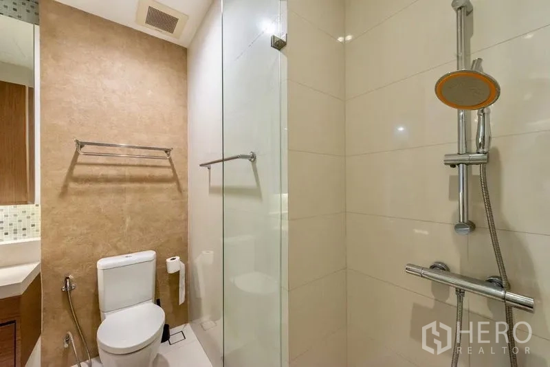 Condominium for rent in Khlong Toei, Bangkok - Modern bathroom with glass-enclosed shower and handheld spray.