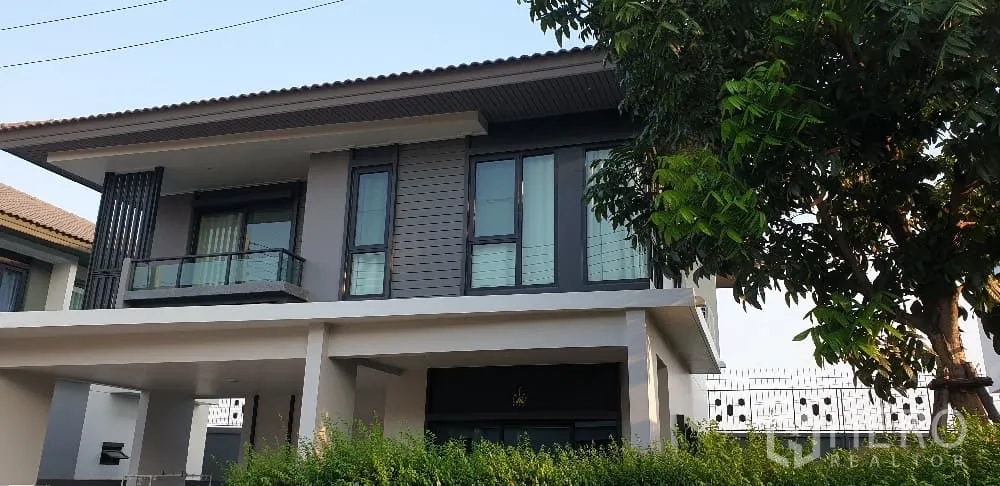 Detached House for rent or sale in Lam Luk Ka, Pathum Thani - Angled exterior view of the two-storey house with glass windows and mature tree.