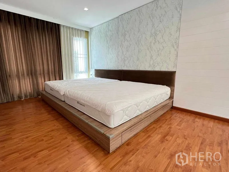 Detached House for sale in Bang Kruai, Nonthaburi - Large bedroom with platform bed, wood floors, and corner windows with drapes.