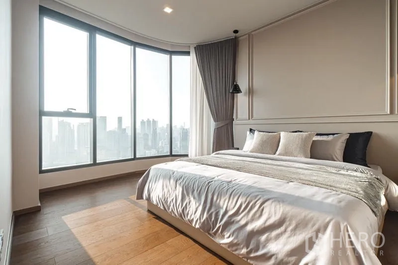 Condominium for rent in Khlong Toei, Bangkok - Bedroom with panoramic city skyline views through large floor-to-ceiling windows.