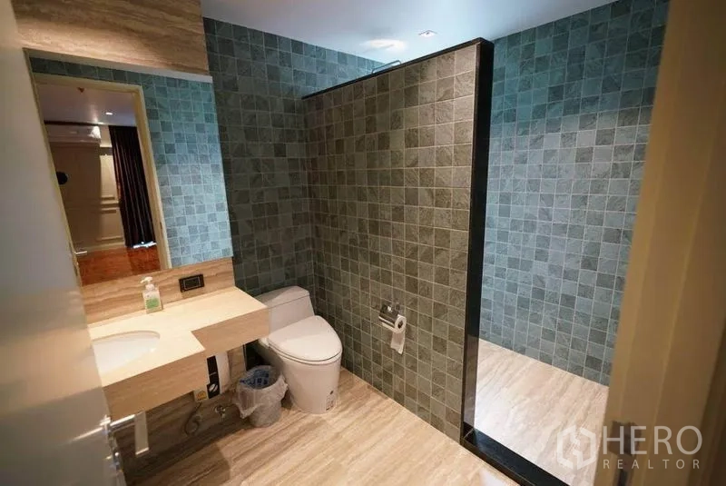 Condominium for rent or sale in Bang Na, Bangkok - Modern bathroom with stone vanity, toilet and a tiled partition leading to a walk‑in shower.