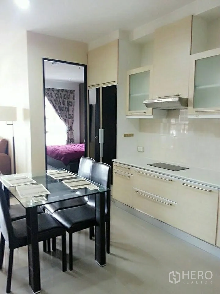 Condominium for rent in Khlong Toei, Bangkok - Open-plan kitchen with glass dining table, built-in cabinets and view into the bedroom.