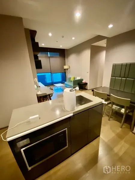 Condominium for rent or sale in Bang Rak, Bangkok - Open-plan living area with kitchen island, teal sofa, dining set and large windows.