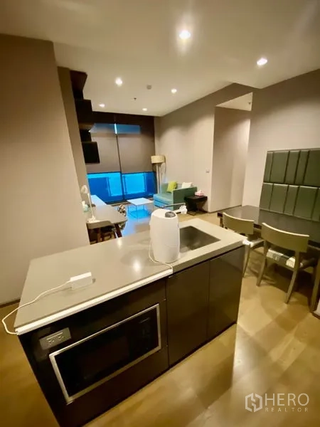 公寓 出租或出售在Bang Rak, Bangkok - 开放式起居区，配有厨房岛台、蓝绿色沙发、餐桌和落地窗。