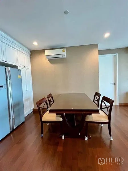 Condominium for rent in Watthana, Bangkok - Dining table for four next to a stainless refrigerator and air conditioner.
