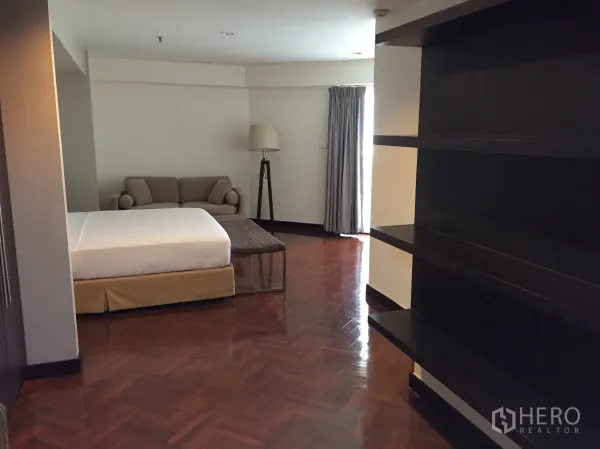 Condominium for rent in Watthana, Bangkok - Spacious bedroom with sofa, floor lamp and open shelving by the window.