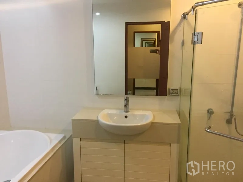 公寓 出租或出售在Khlong Toei, Bangkok - 浴室设洗手台与镜子，配浴缸及玻璃淋浴间。