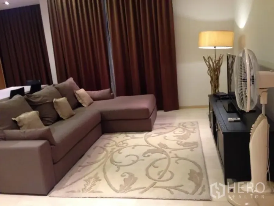 Condominium for sale in Bang Rak, Bangkok - Cozy living room with L-shaped sofa, floor lamp, TV console and full-length curtains.