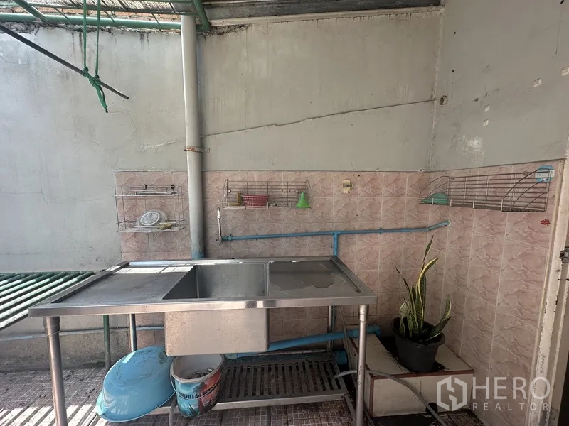 Shophouse for rent or sale in Phra Khanong, Bangkok - Simple rear wet kitchen with stainless steel double sink, wall racks, and tiled splashback.