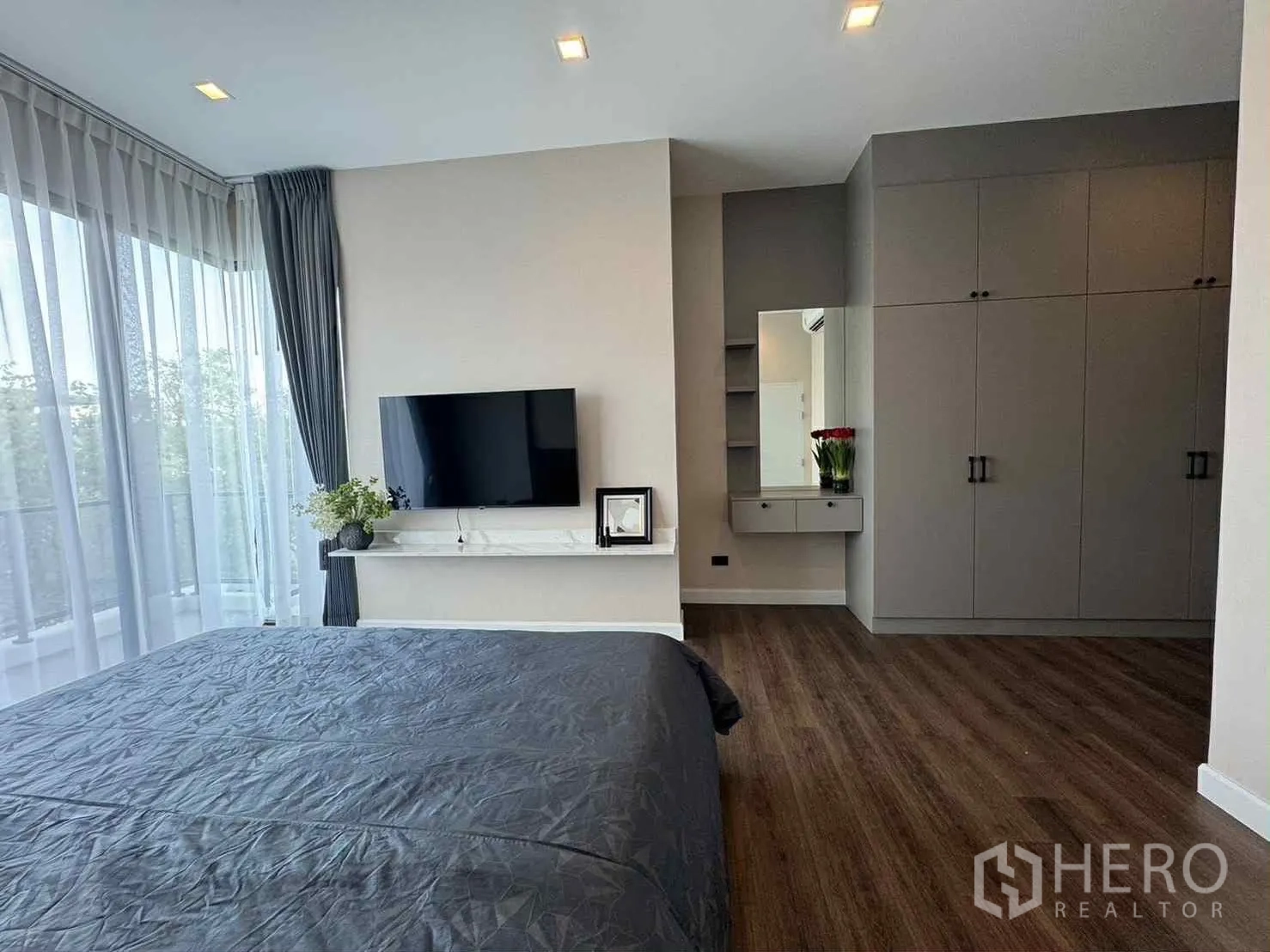 บ้านเดี่ยว for rent in Bang Phli, Samut Prakan - ห้องนอนกว้างมีผนังติดทีวี ตู้เสื้อผ้า โต๊ะเครื่องแป้ง และหน้าต่างมุมพร้อมม่าน.