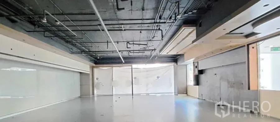 Retail Space for rent - Open-plan retail interior with exposed black ceiling, visible ductwork and wiring, smooth light floor, and covered floor-to-ceiling glass frontage ready for fit-out.