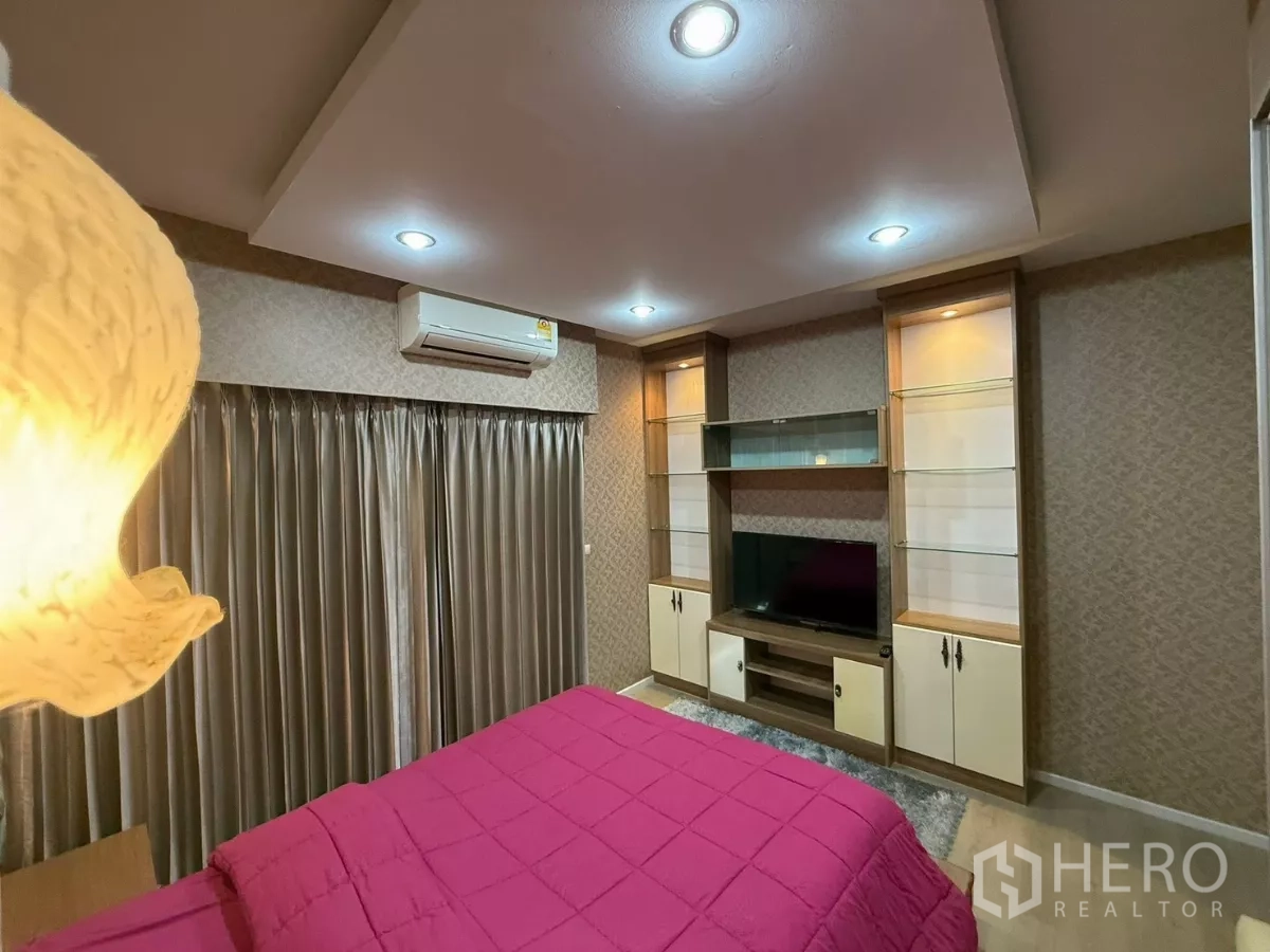 Townhouse for rent in Suan Luang, Bangkok - Third bedroom alternate angle with TV unit, shelves and long curtains.