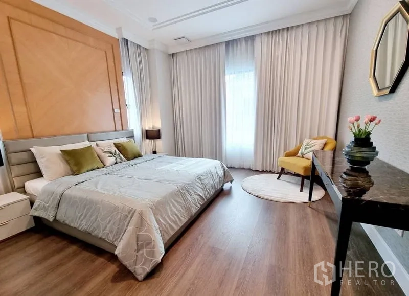Detached House for rent in Saphan Sung, Bangkok - Cozy bedroom with wood flooring, large bed, accent wall, and reading chair.