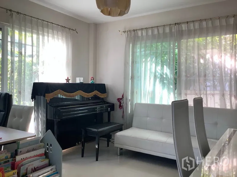 Detached House for rent in Bang Kapi, Bangkok - Bright living room with white sofa, upright piano and sheer curtains overlooking greenery.