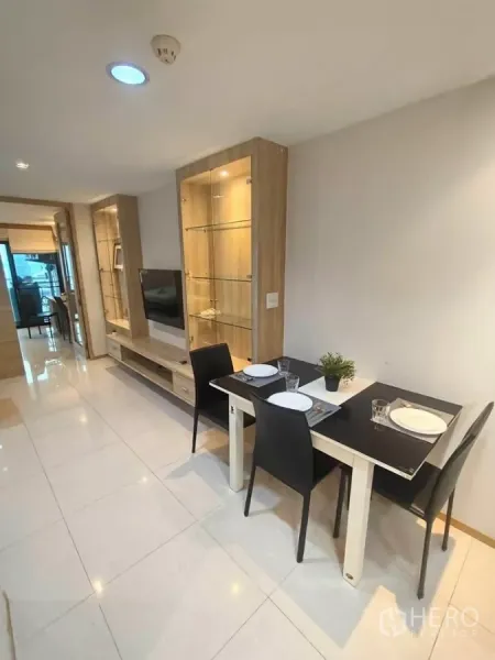 Condominium for rent in Khlong Toei, Bangkok - Open-plan living and dining area with glass display cabinets, wall-mounted TV, and a two-seat table in a modern Bangkok condo.