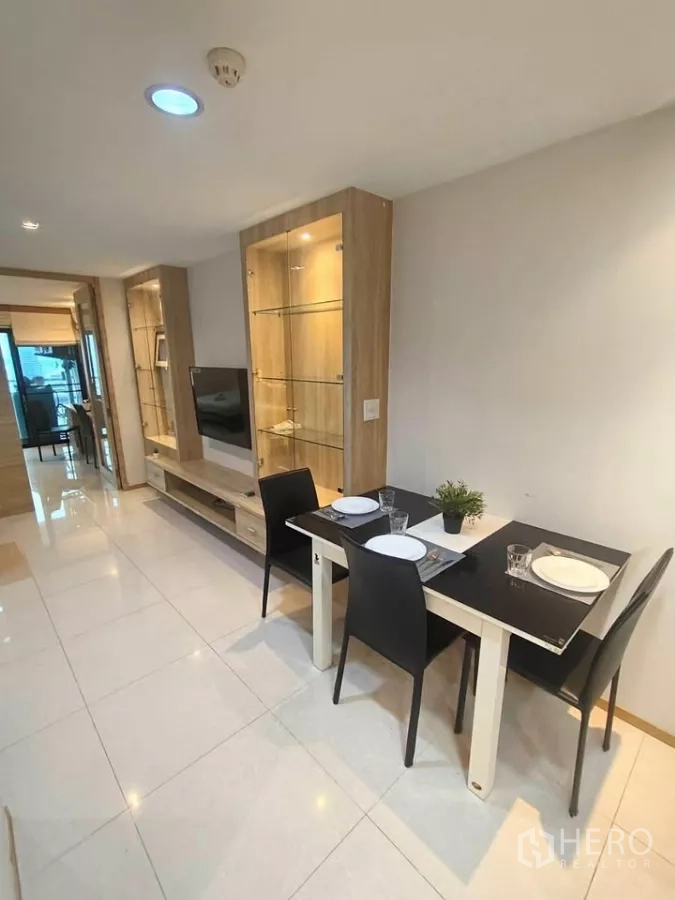 Condominium for rent in Khlong Toei, Bangkok - Open-plan living and dining area with glass display cabinets, wall-mounted TV, and a two-seat table in a modern Bangkok condo.
