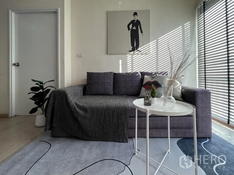Condominium for rent in Khlong Toei, Bangkok - Close-up of sofa corner with side table and glass decor by sunlit blinds.