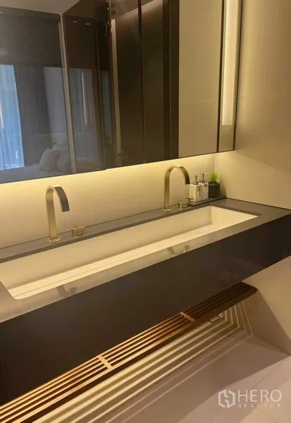Condominium for rent in Khlong Toei, Bangkok - Elegant double vanity with brass faucets and a backlit mirror.