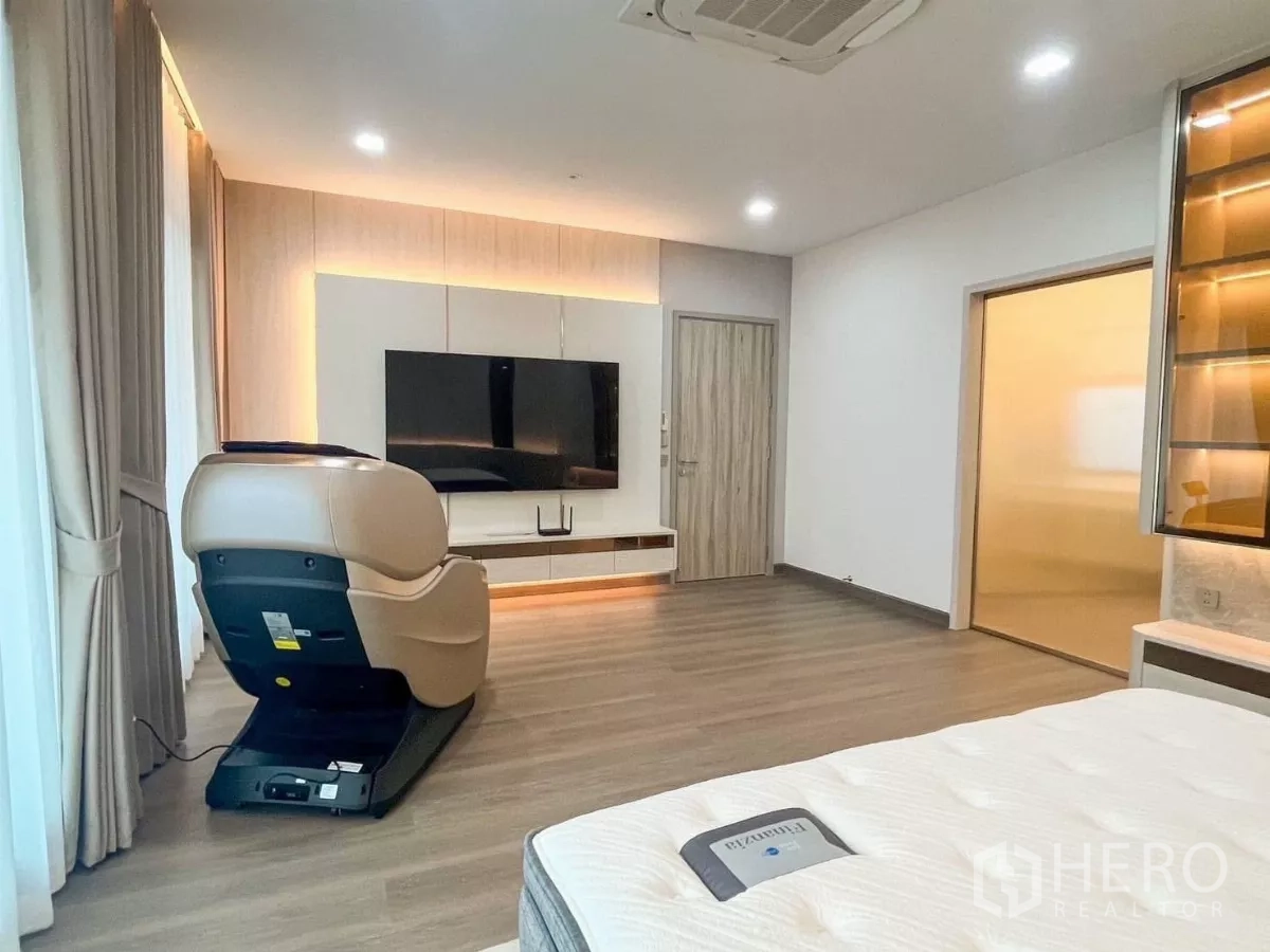 Detached House for rent or sale in Prawet, Bangkok - Spacious master bedroom with wood floors, TV wall, large windows and a massage chair.