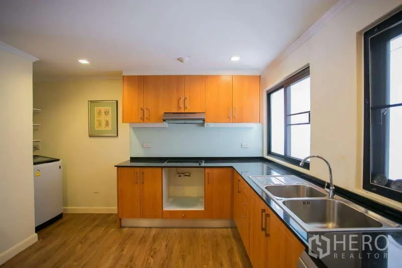 Condominium for rent or sale in Watthana, Bangkok - Kitchen corner with double sink, black countertops and glass backsplash.