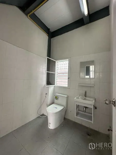 Warehouse for rent in Pak Kret, Nonthaburi - Clean tiled restroom with window, sink, and toilet inside the facility.