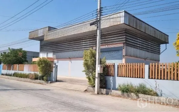 货栈 出售在Pathum Thani - 转角视角的金属外墙仓库，围栏与大型卷帘门清晰可见。