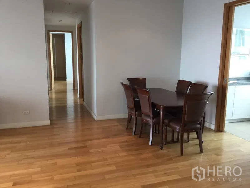 Condominium for rent in Khlong Toei, Bangkok - Dining area with six-seat wooden table next to the doorway leading to the separate kitchen.