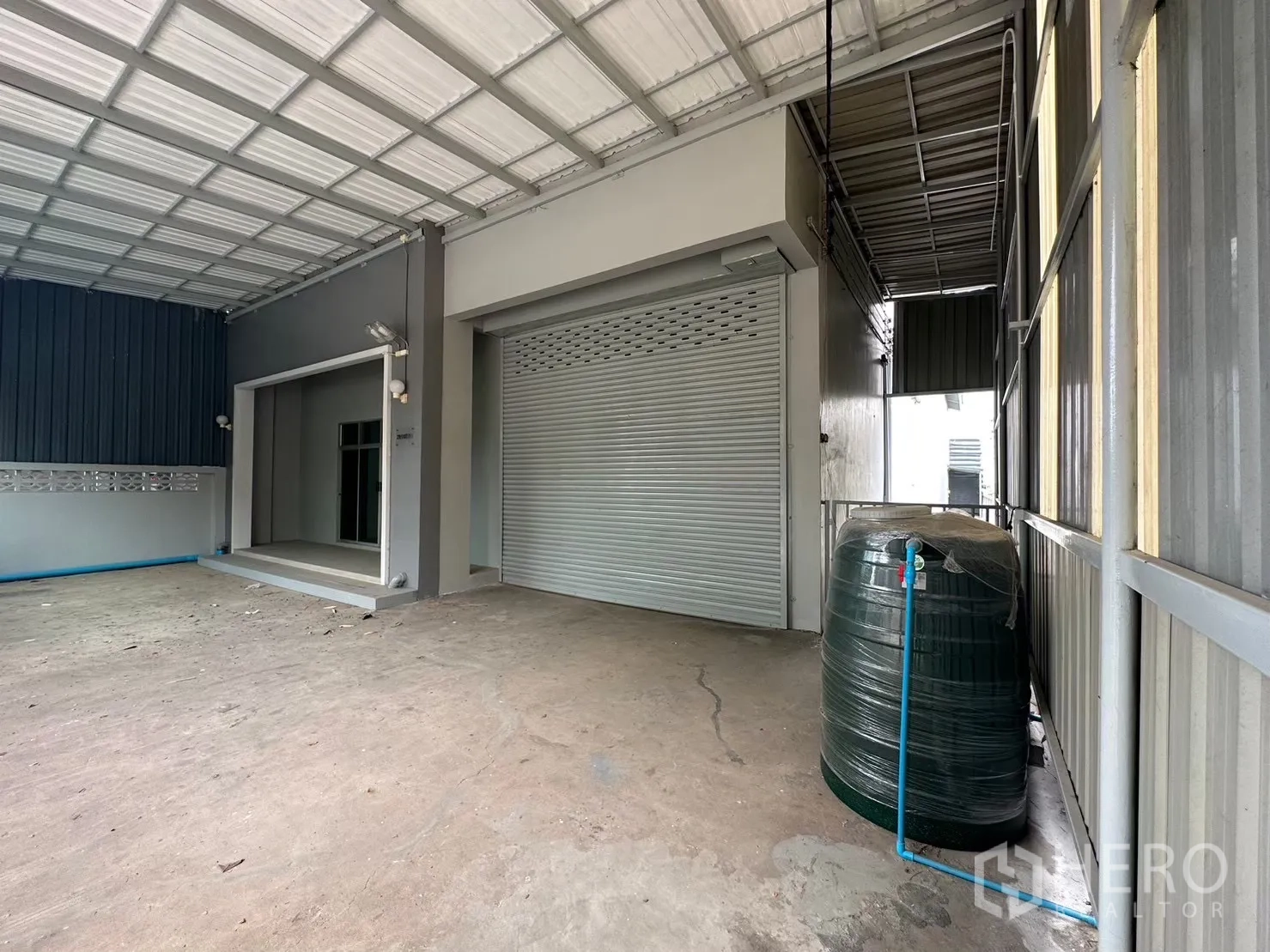 Factory for rent in Bang Bua Thong, Nonthaburi - Wide roller shutter and sheltered loading bay with a water tank.