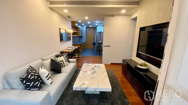 Condominium for sale in Khlong Toei, Bangkok - Living area facing TV wall and open galley kitchen with warm wood floors.