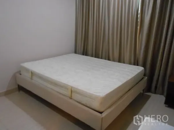 Condominium for rent in Watthana, Bangkok - Second bedroom with double mattress, beige bed frame, and floor-to-ceiling curtains.