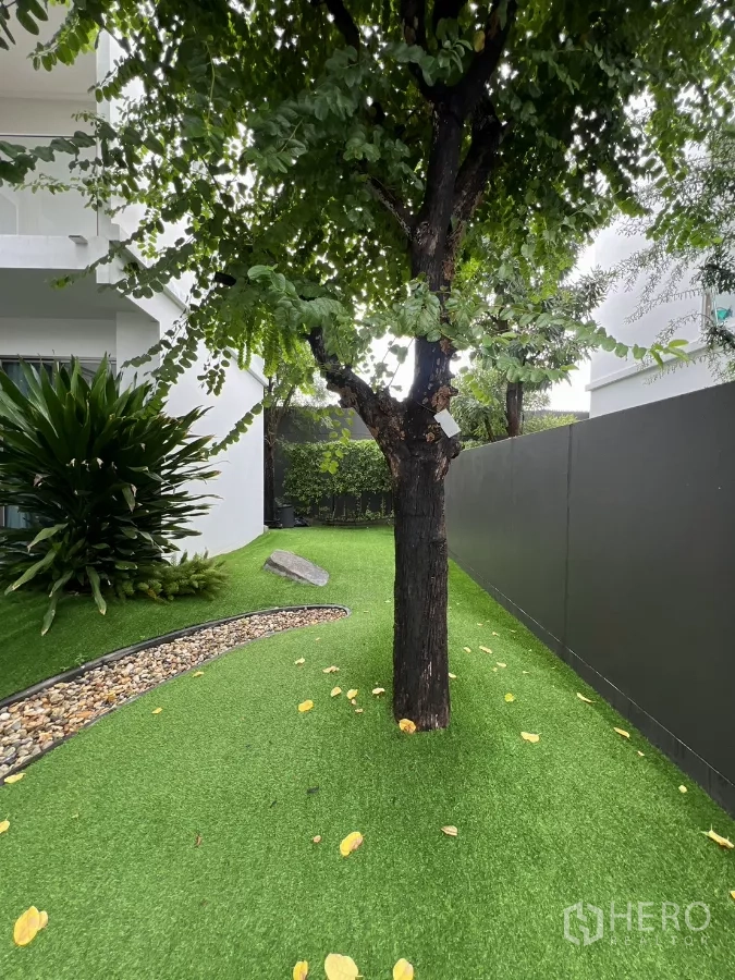Detached House for rent in Saphan Sung, Bangkok - Private side yard with mature tree, artificial grass and a high privacy fence.